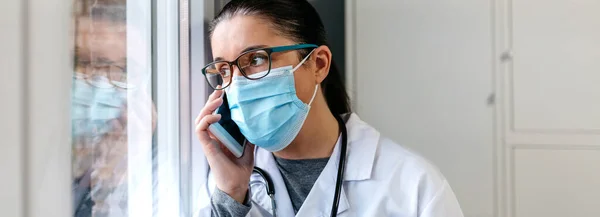 Médecin féminin parlant sur le téléphone portable regardant par la fenêtre — Photo