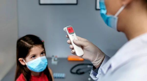 Ärztin schaut auf Infrarot-Thermometer, nachdem sie einem Mädchen die Temperatur genommen hat — Stockfoto