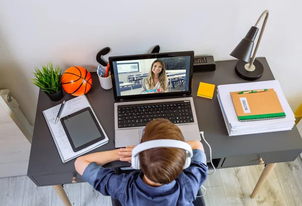 Vista superior de niño irreconocible con auriculares que reciben clase en casa con el ordenador portátil —  Fotos de Stock