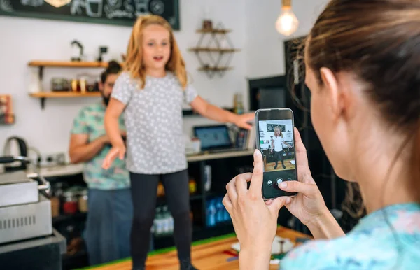 Anne, kahve dükkanında çalışırken kızını cep telefonuyla dans ederken kaydediyor. — Stok fotoğraf