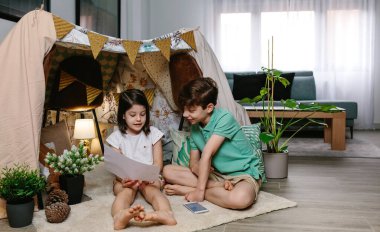 Boy and girl playing in a diy tent at home clipart