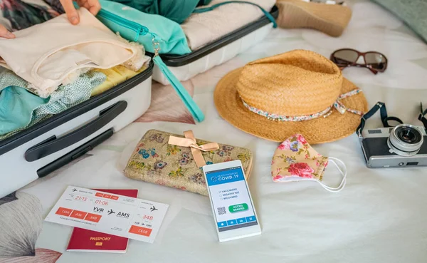 Mulher preparando mala para férias e telefone celular com passe verde vívido — Fotografia de Stock