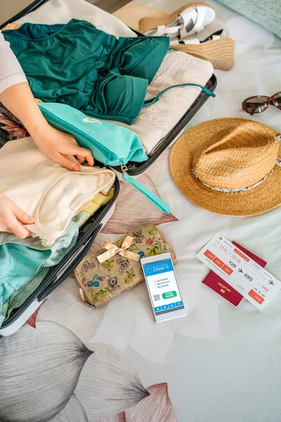 Kvinna förbereda resväska för semester och mobiltelefon med covid grönt pass — Stockfoto