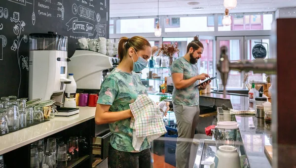 Garçonete com óculos de limpeza máscara enquanto seu colega de trabalho trabalha com tablet — Fotografia de Stock