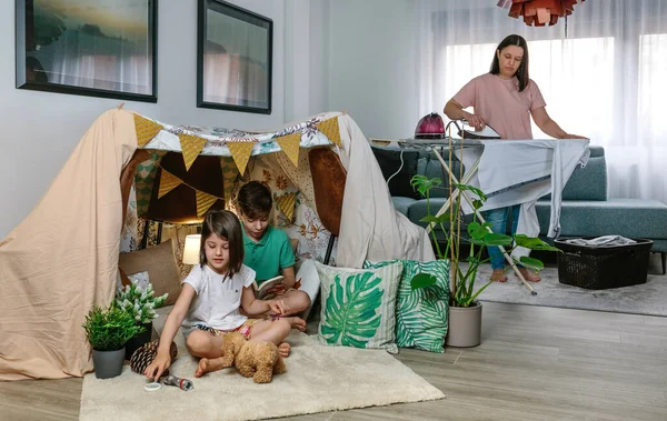 Madre planchando mientras sus hijos juegan al camping en casa —  Fotos de Stock