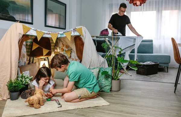 Padre planchando mientras sus hijos juegan al camping en casa —  Fotos de Stock