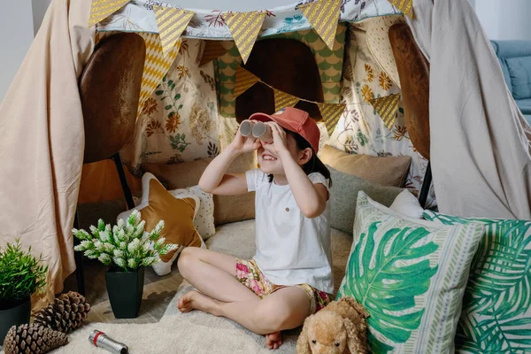 Девушка играет с картонным биноклем во время кемпинга дома — стоковое фото