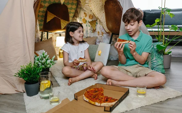 Bambini che mangiano pizza e limonata mentre si accampano a casa — Foto Stock