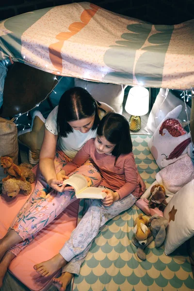 Vista superior de la madre y la hija teniendo una fiesta de pijama leyendo un libro —  Fotos de Stock