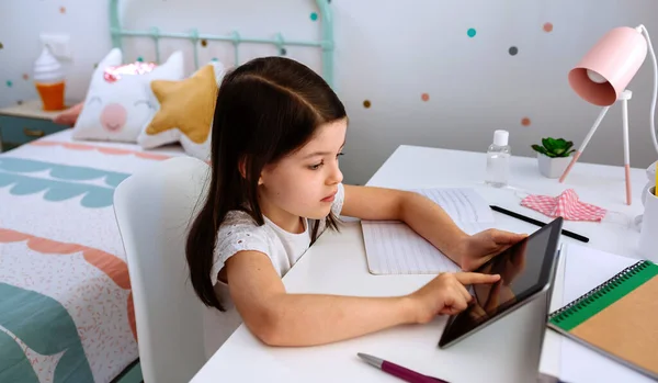 Chica estudiando en casa con la tableta y la máscara en la mesa — Foto de Stock