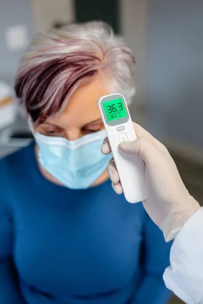 Femme âgée sans fièvre dont la température est prise avec un thermomètre infrarouge — Photo