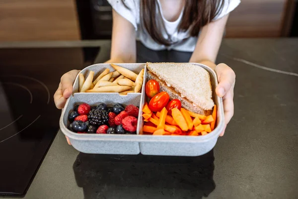 Fille méconnaissable montrant boîte à lunch remplie d'aliments sains — Photo