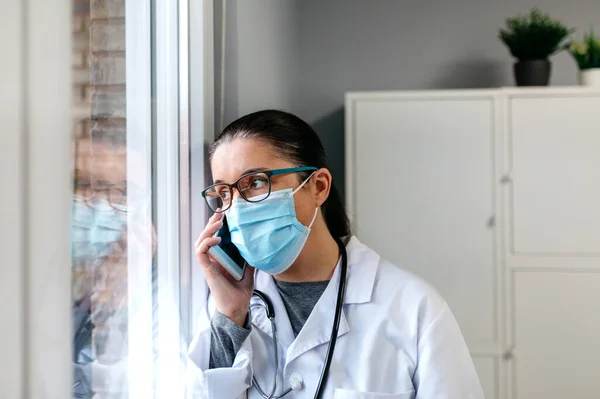 Ärztin telefoniert mit dem Handy und schaut aus dem Fenster — Stockfoto