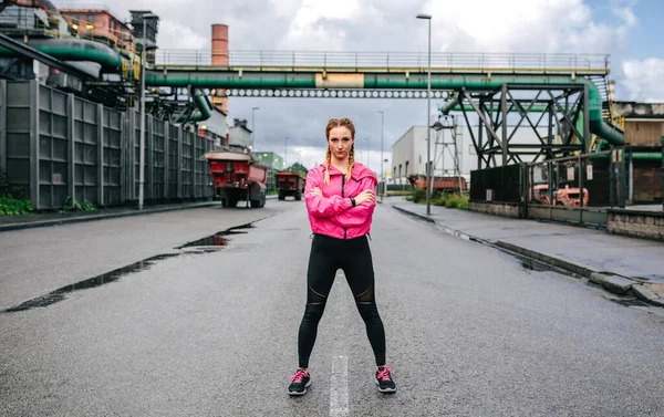 Sportos nő néz kamera pózol előtt egy gyár — Stock Fotó
