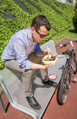 Young business man eating at lunch break outdoors clipart