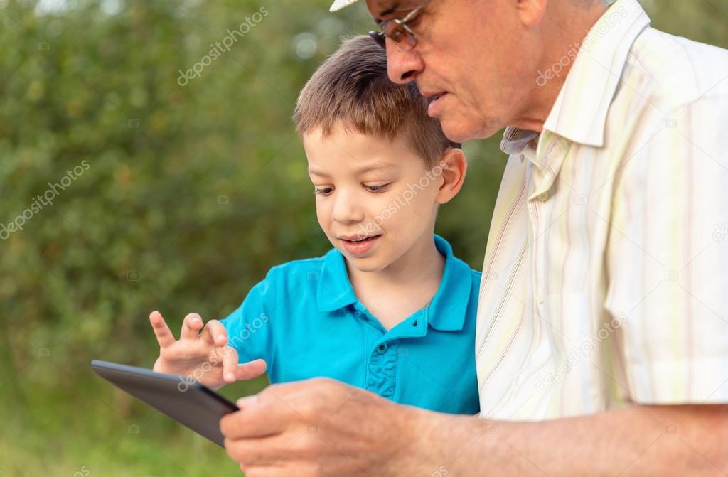 Grandchild and grandfather using a tablet outdoors