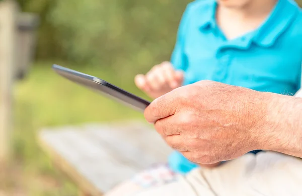 Mãos de avô usando um tablet com granchild ao ar livre — Fotografia de Stock