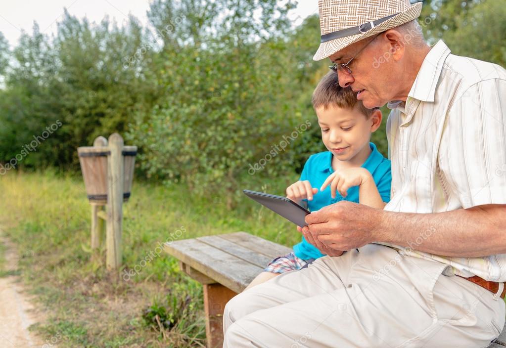 Grandchild and grandfather using a tablet outdoors