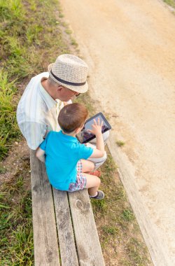 Grandchild and grandfather using a tablet outdoors clipart