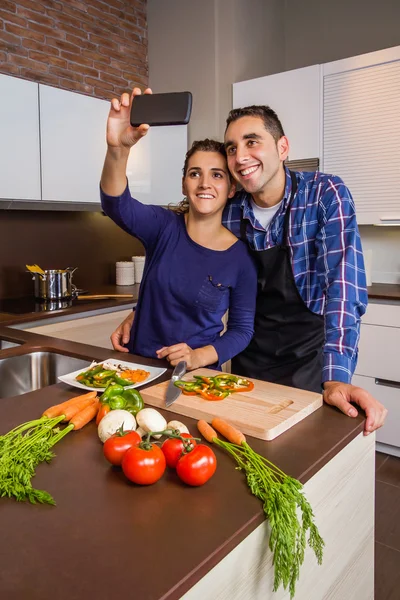 Пара на кухні готує і приймає селфі зі смартфоном — стокове фото