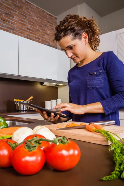 Menina em casa cozinha procurando receita com um tablet eletrônico — Fotografia de Stock