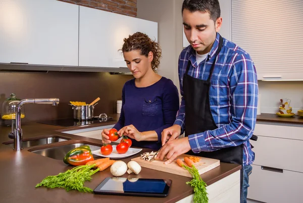 Casal em casa cozinha procurando receita com um tablet eletrônico — Fotografia de Stock