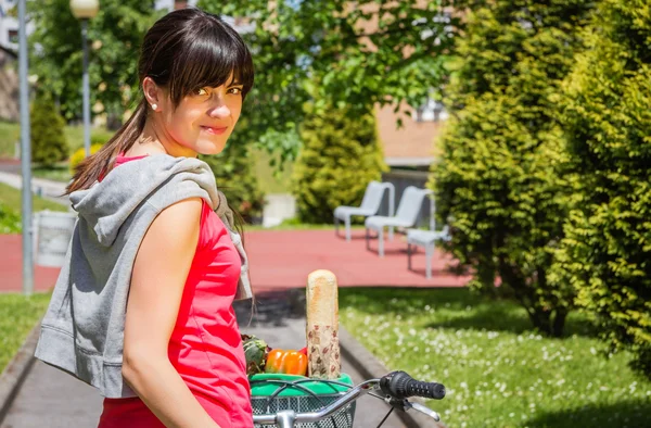 Молода спортивна жінка з продуктами в кошику велосипеда — стокове фото