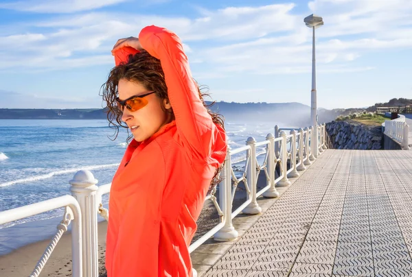 Chica joven calentándose antes de correr en un paseo marítimo — Foto de Stock