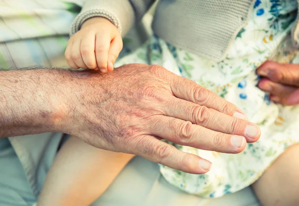 Baby girl touching hand of senior man — Stok Foto