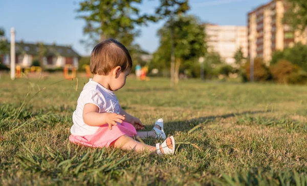 Glückliches Mädchen spielt sitzend auf einem Rasenpark — Stockfoto