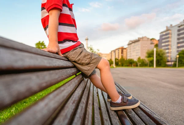 Boy legs sitting on the top of bench park relaxing — Stock Photo, Image