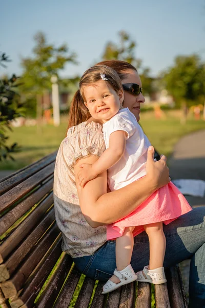 Bebê menina de pé em um banco abraçando a mulher — Fotografia de Stock