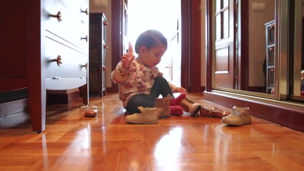 Meisje van de baby proberen zetten schoenen zitten over houten vloer — Stockvideo