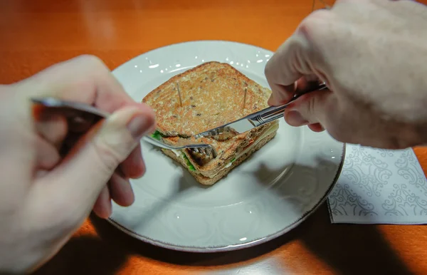 Mann schneidet Sandwich mit Gabel und Messer — Stockfoto