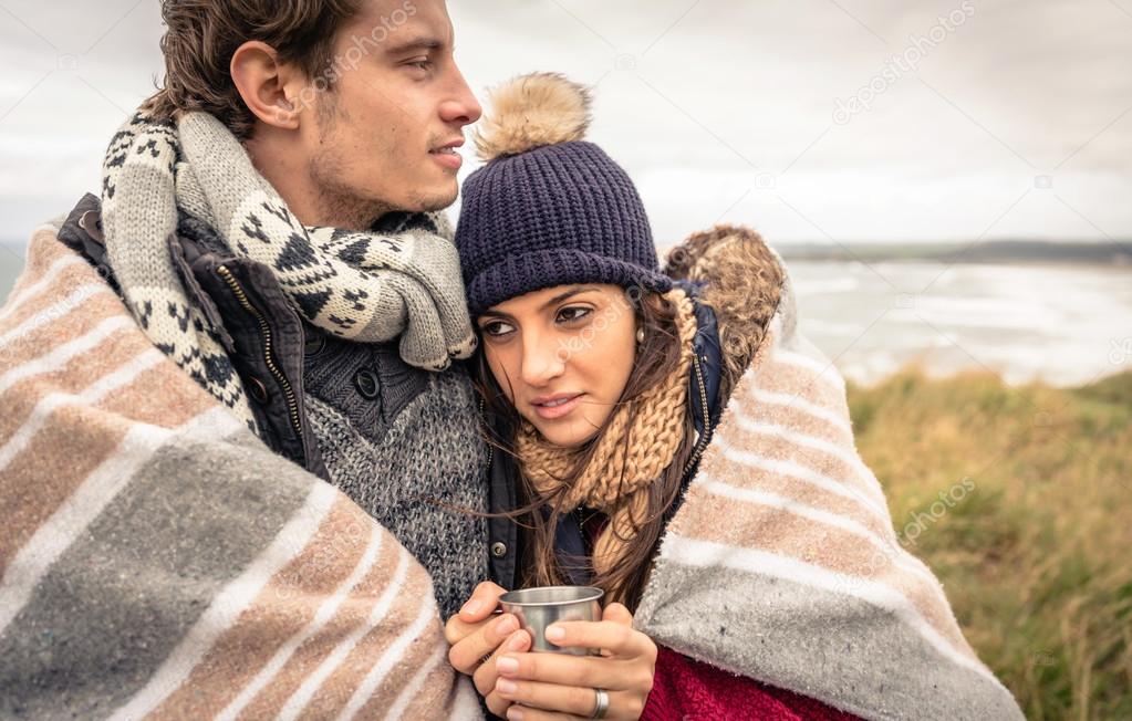 Young couple embracing outdoors under blanket in a cold day