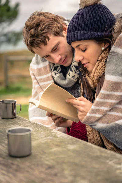 Jovem casal sob cobertor leitura livro ao ar livre em um dia frio — Fotografia de Stock