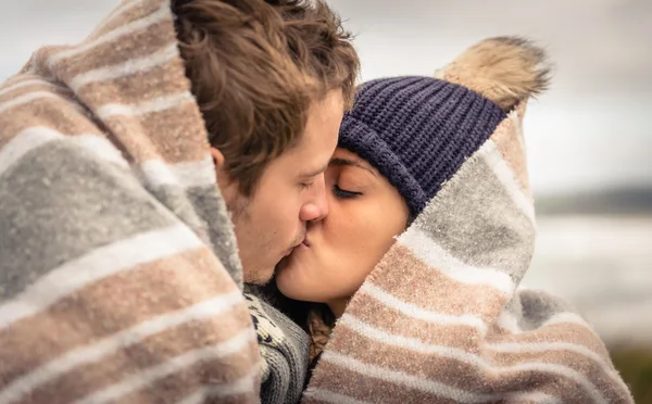 Jong koppel zoenen buitenshuis onder deken in een koude dag — Stockfoto