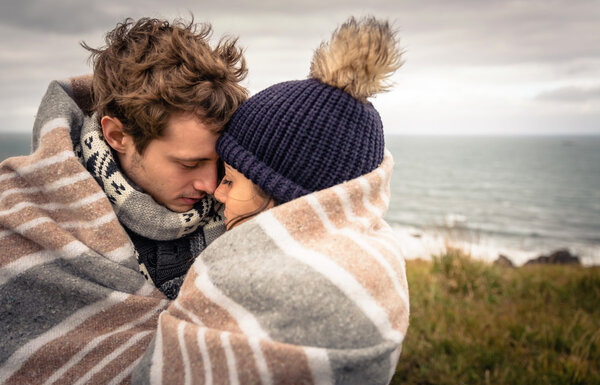 Young couple embracing outdoors under blanket in a cold day