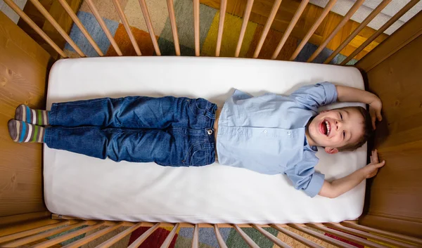 Happy boy lying in a cot with arms and legs stretched — Stock Photo, Image