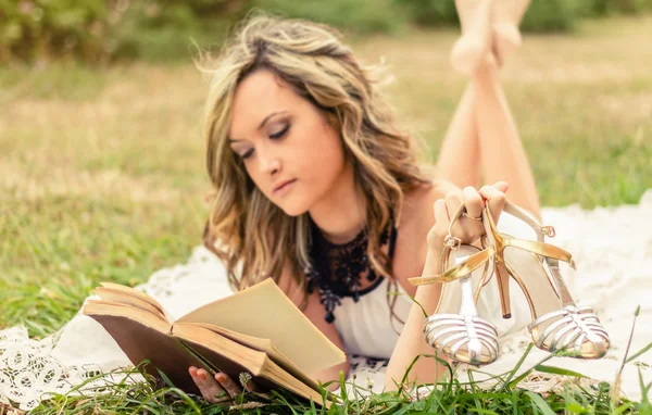 Romantic girl with shoes in the hand reading a book outdoors — Stock Photo, Image