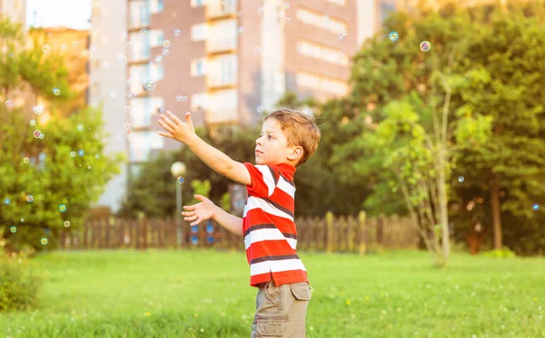 Menino feliz brincando com bolhas de sabão no parque — Fotografia de Stock