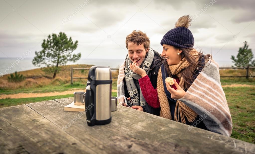 Young couple under blanket eating muffin outdoors in a cold day