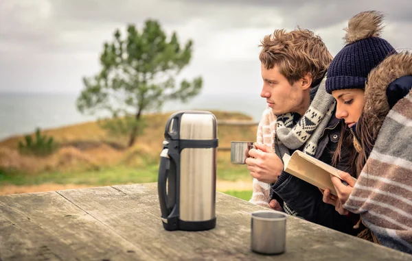 Pareja joven bajo manta leyendo libro al aire libre en un día frío —  Fotos de Stock