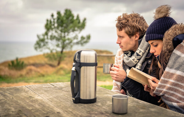 Young couple under blanket reading book outdoors in a cold day