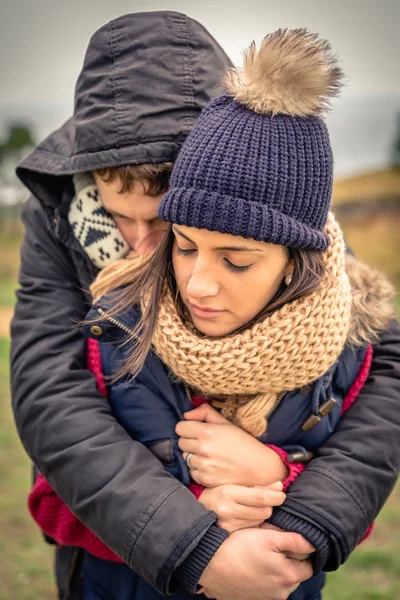 Young couple with hat and scarf embracing outdoors — Stock Photo, Image