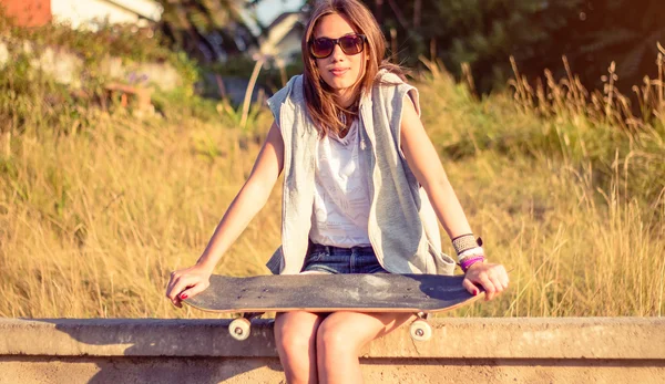 Mladá dívka s skateboard sedí přes zeď na léto — Stock fotografie