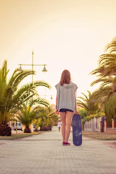 Vista posteriore della ragazza con uno skateboard all'aperto in estate — Foto Stock