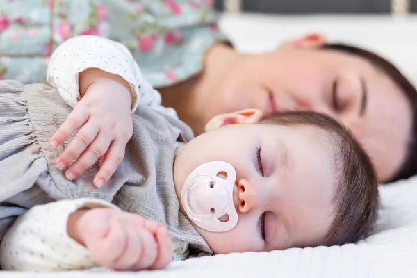 Jonge moeder en haar babymeisje slaapt in het bed — Stockfoto