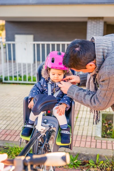 Padre cerrando el casco a su hija sentada en el asiento de la bicicleta — Foto de Stock