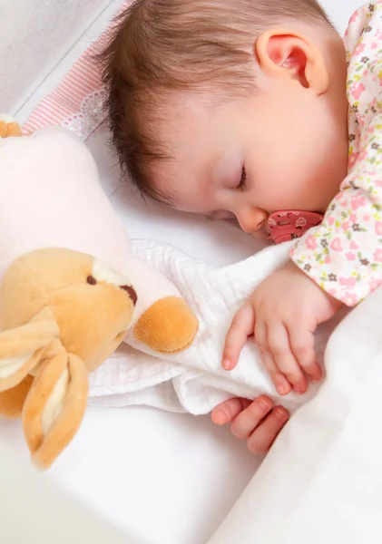 Baby flicka sover i en barnsäng med napp och leksak — Stockfoto